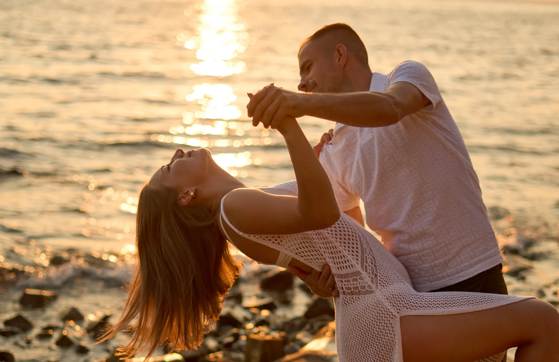 Couple dancing by the sea at golden hour sunset